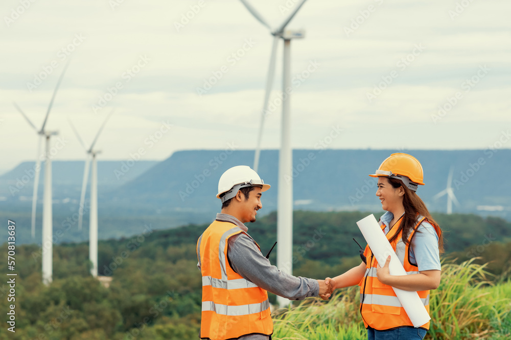 Male and female engineers working on a wind farm atop a hill or mountain in the rural. Progressive i