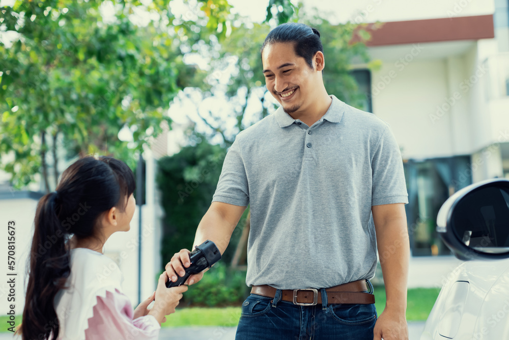 Progressive father and daughter returned from school in electric vehicle that is being charged at ho