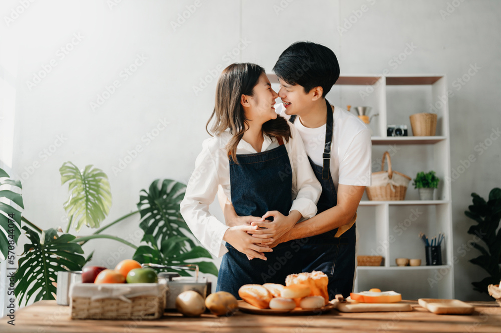 A man in the kitchen preparing a meal with Bread and fruit in cozy kitchen while his wife hugging hi