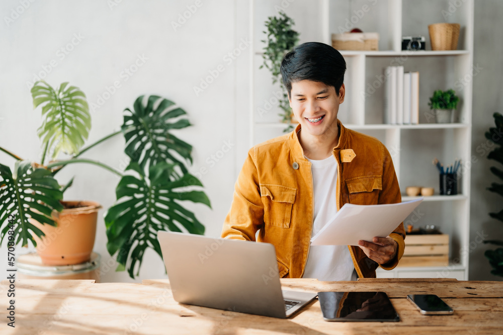 Young business man working at home office with laptop, tablet and taking notes on the paper.