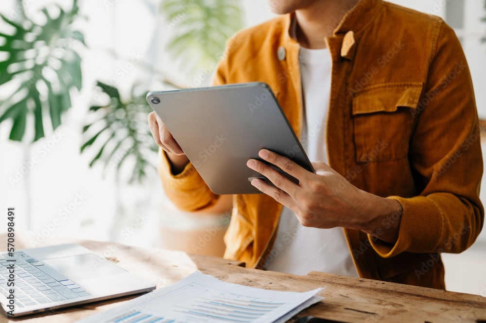 Young business man working at home office with laptop, tablet and taking notes on the paper.