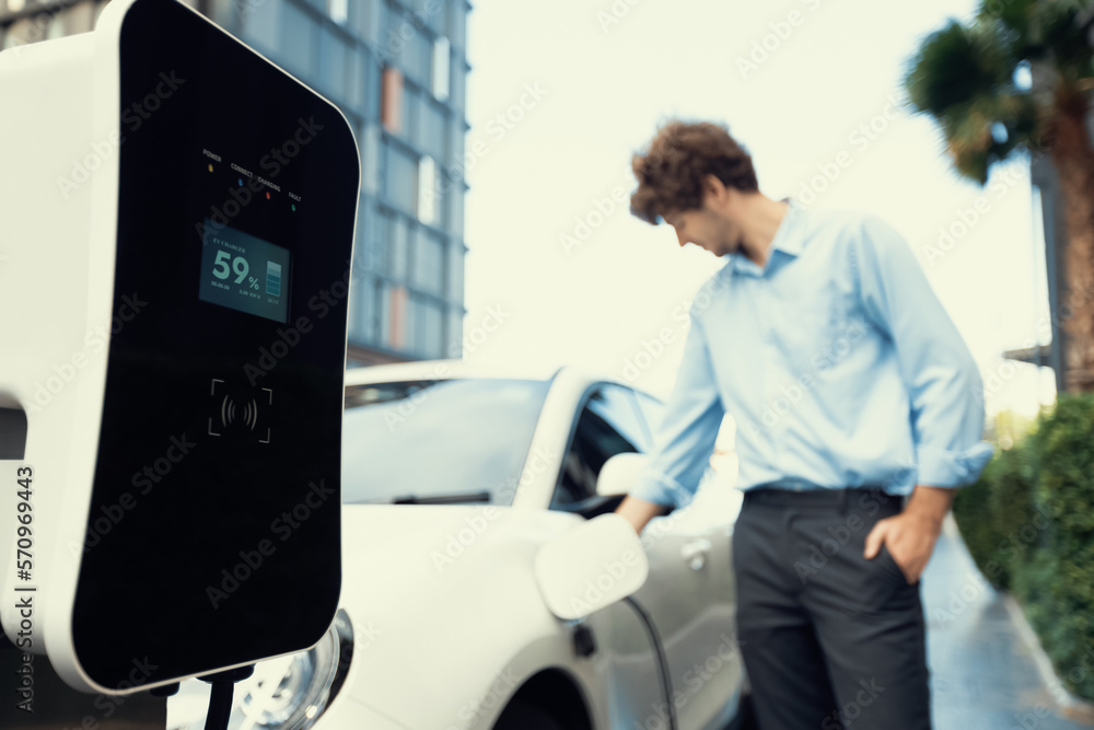 Focus public EV charging station in city residential area with blur background of businessman chargi