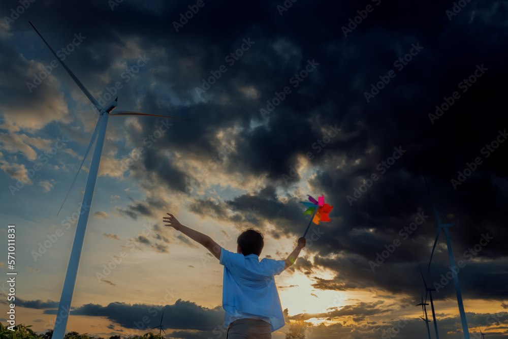 Progressive young asian boy playing with wind pinwheel toy in the wind turbine farm, green field ove