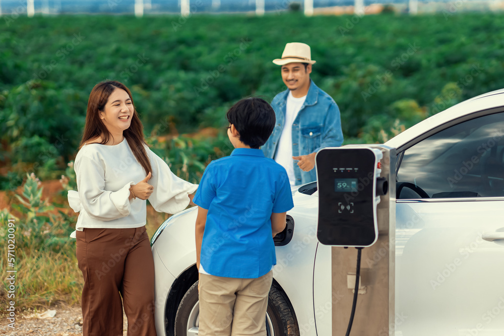 Concept of progressive happy family enjoying their time at wind farm with electric vehicle. Electric