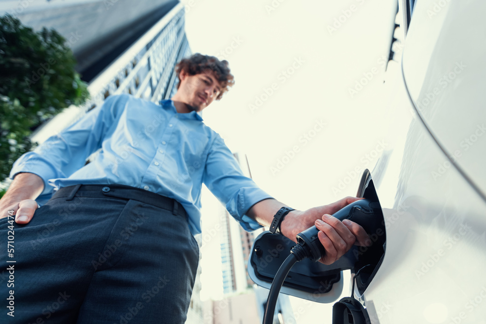 Fisheye view focus on hand insert EV charger plug into electric car with blur background of progress