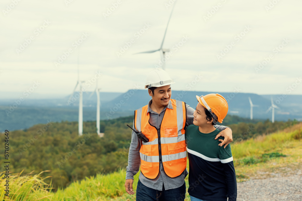 Engineer with his son on a wind farm atop a hill or mountain in the rural. Progressive ideal for the