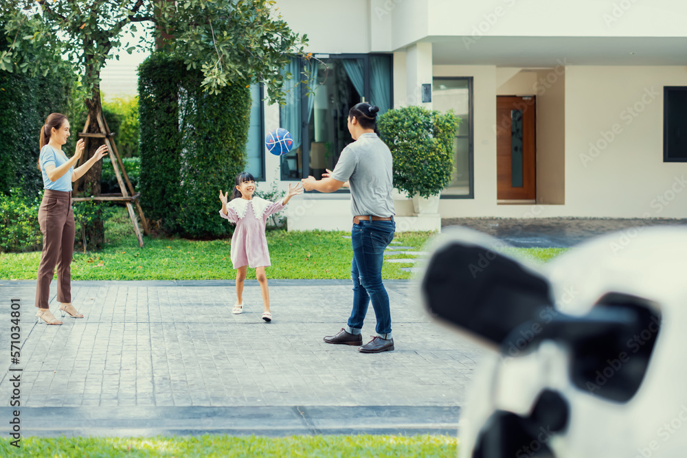 Progressive young happy family with electric vehicle and home backyard charging station. Green and c