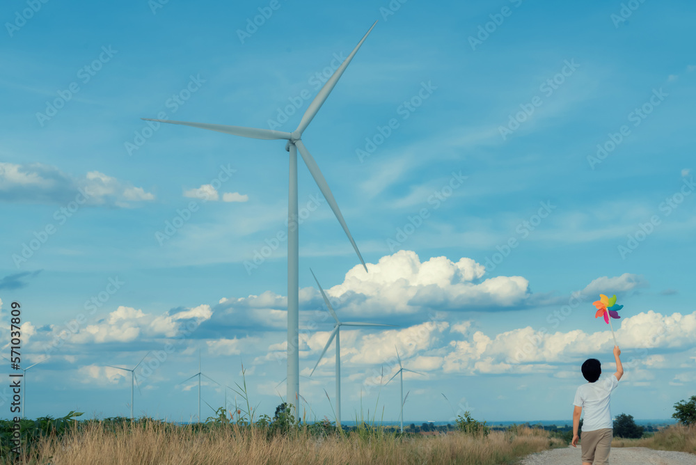 Progressive young asian boy playing with wind pinwheel toy in the wind turbine farm, green field ove