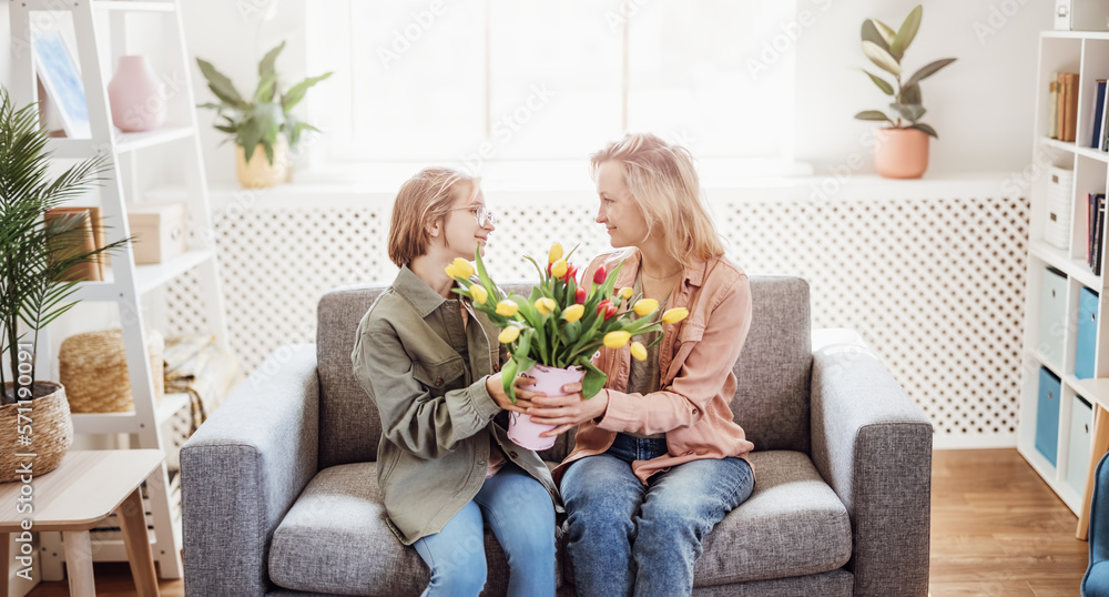 Mother and daughter sitting on the sofa with tulips in their hands indoor.