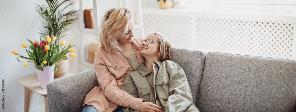 Mother and daughter sitting on the sofa indoor and embracing.