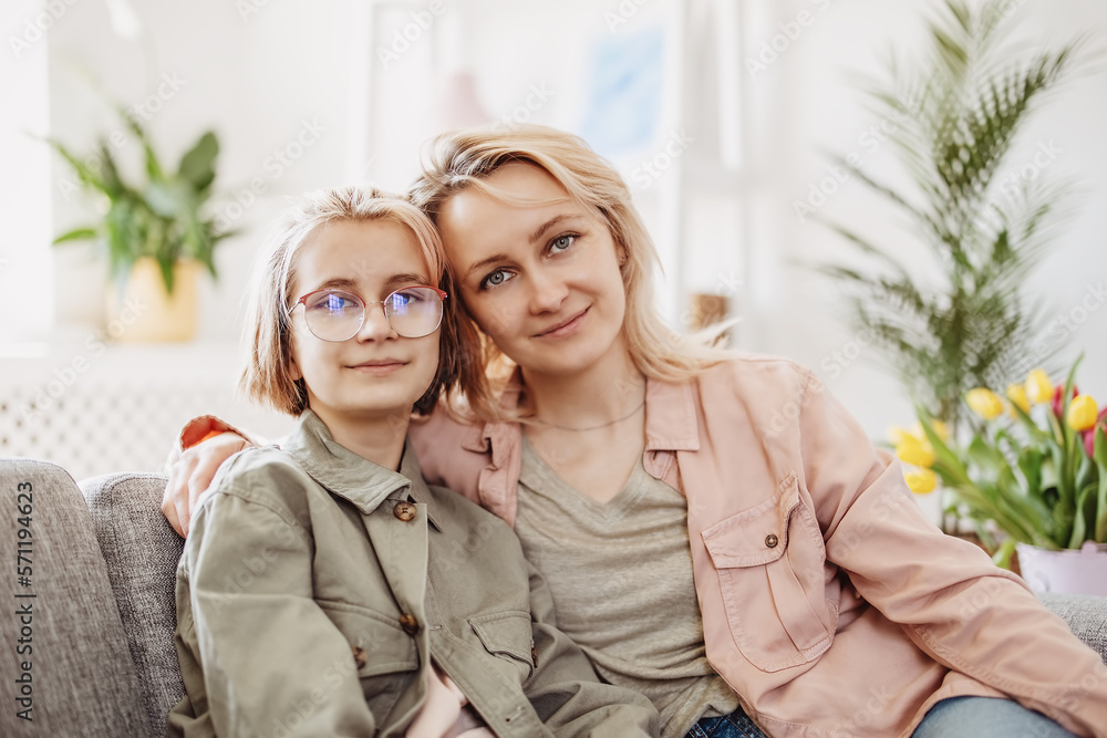 Mother and daughter sitting on the sofa indoor and embracing.