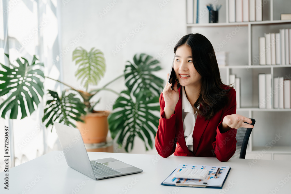 Business asian woman Talking on the phone and using a laptop with a smile while sitting at office