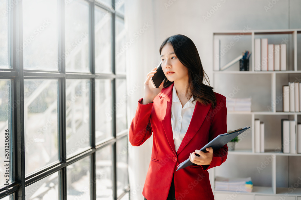 Business asian woman Talking on the phone and using a laptop with a smile while sitting at office