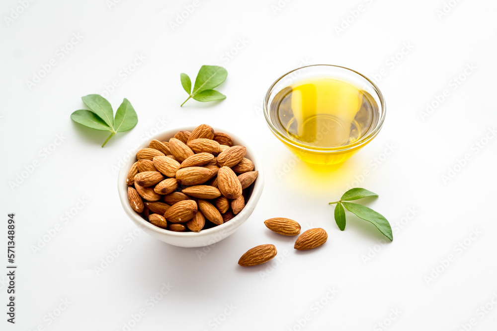 Sweet almond oil in glass jar and almond seeds with green leaf