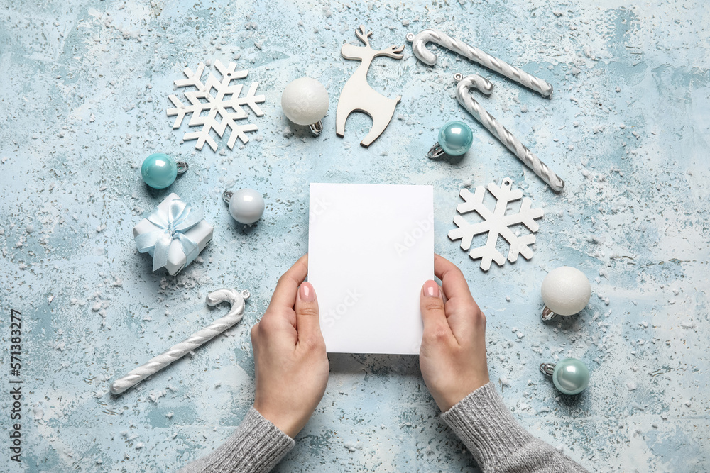 Woman holding paper sheet, gift and Christmas decor on blue background