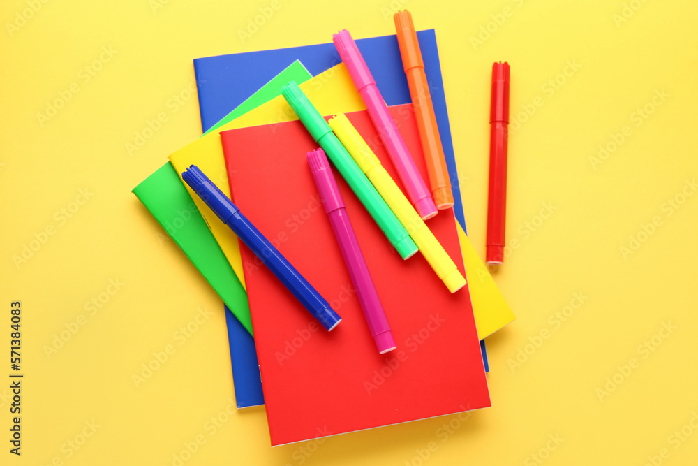 Notebooks and felt-tip pens on yellow background