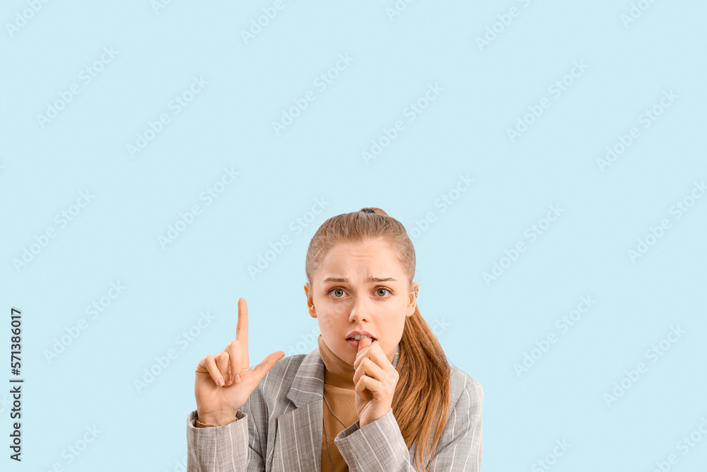 Young businesswoman biting nails and pointing at something on blue background