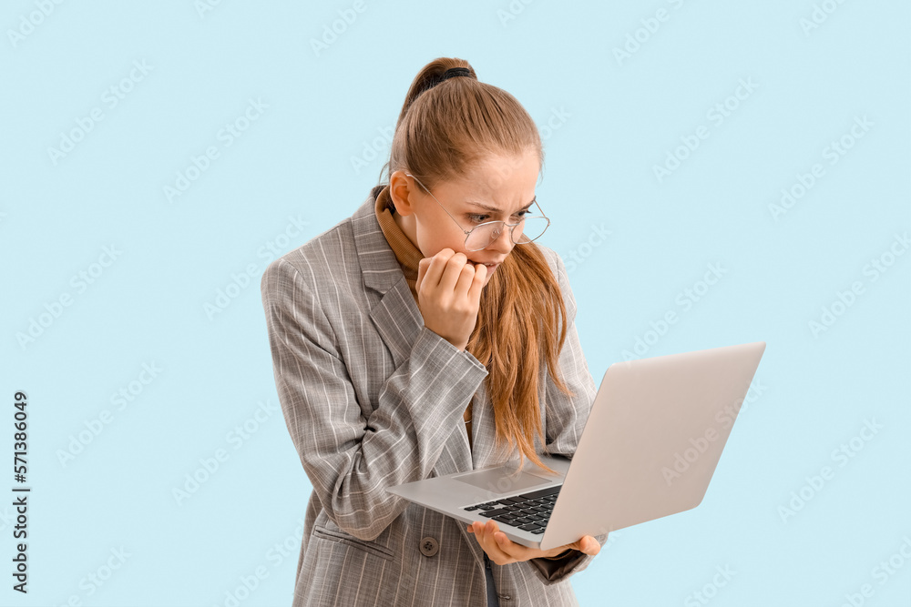 Young businesswoman with laptop biting nails on blue background