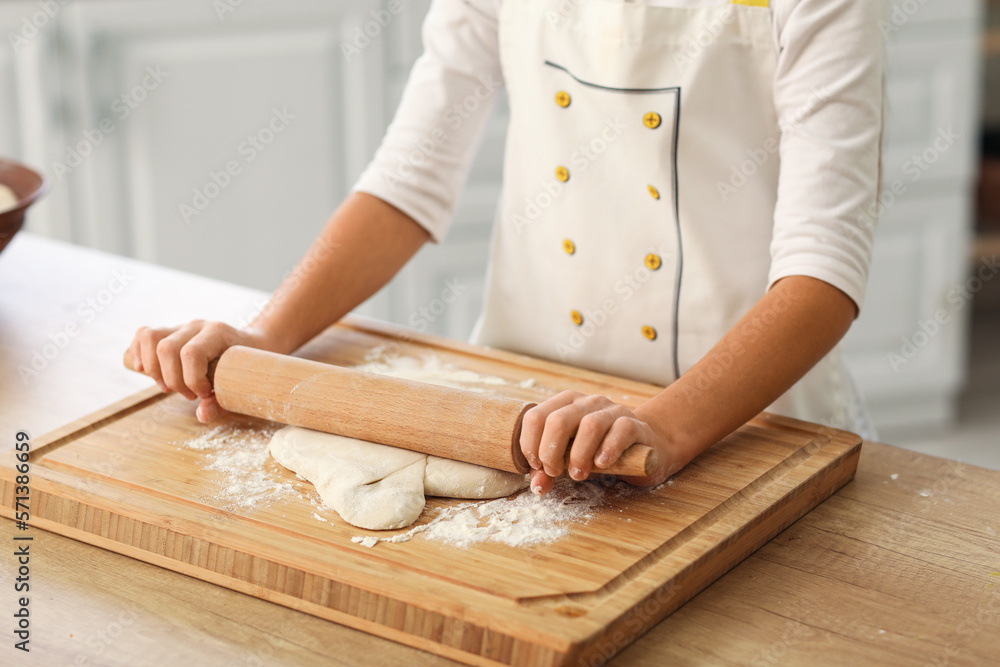 Little baker rolling out dough at table in kitchen, closeup