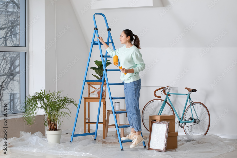 Young woman with paint roller and ladder at home