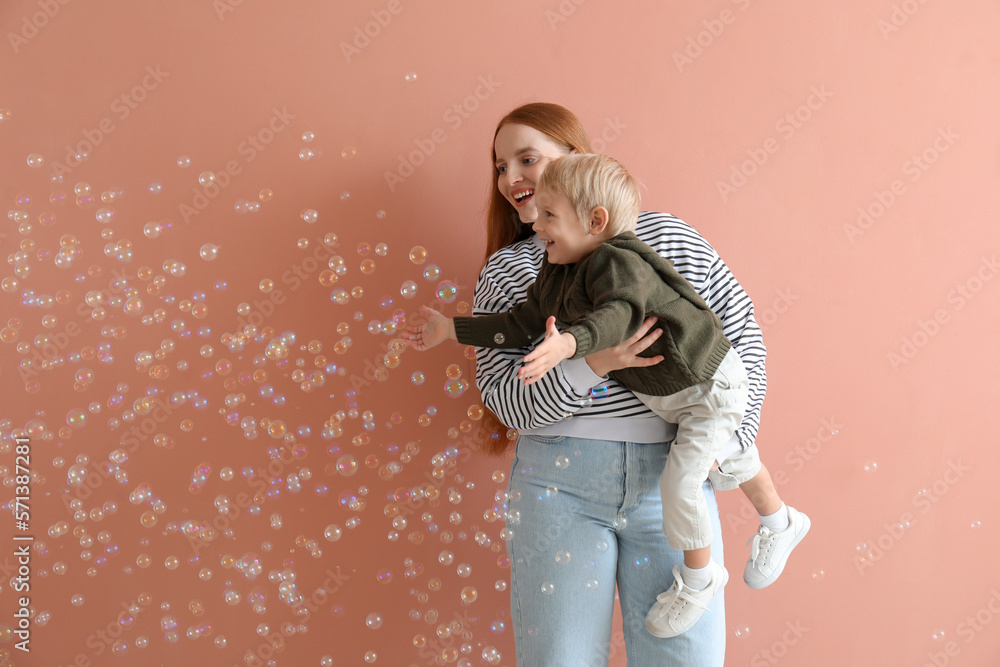 Happy mother with her little son and soap bubbles on pink background