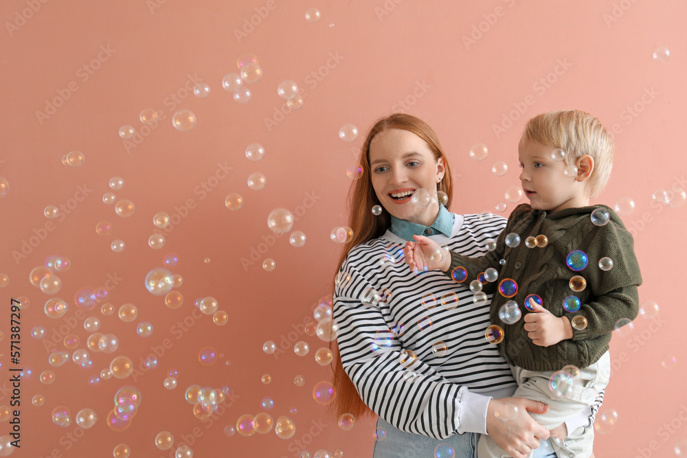 Happy mother with her little son and soap bubbles on pink background