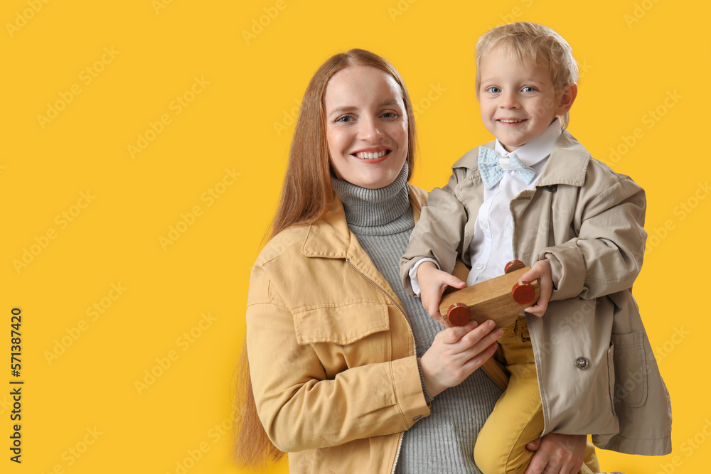 Happy mother and her little son with toy car on yellow background