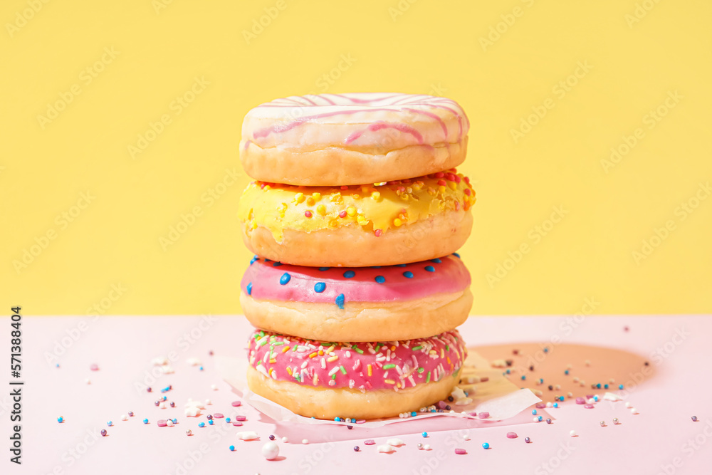 Parchment with different delicious donuts on pink table near yellow wall