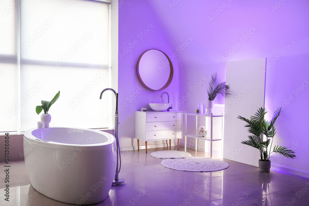 Interior of stylish bathroom with bathtub, houseplants, mirror and neon lighting