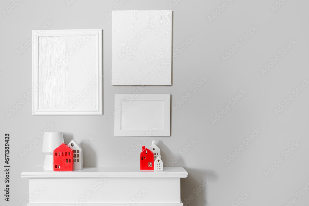 Interior of room with glowing house candle holders on fireplace and blank frames near grey wall