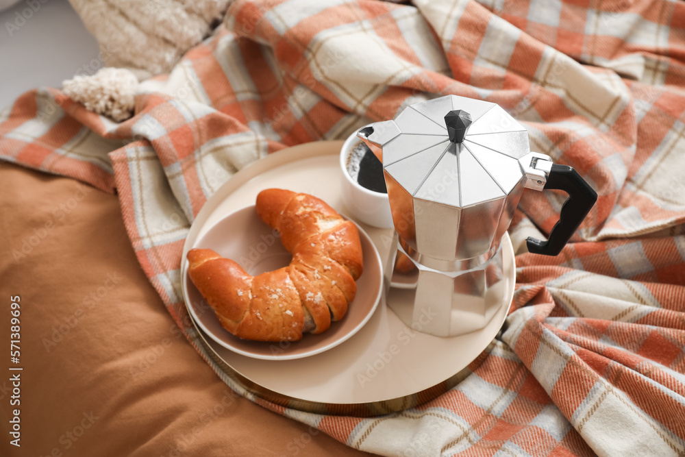 Plate with geyser coffee maker, delicious croissant and cup of espresso on bed