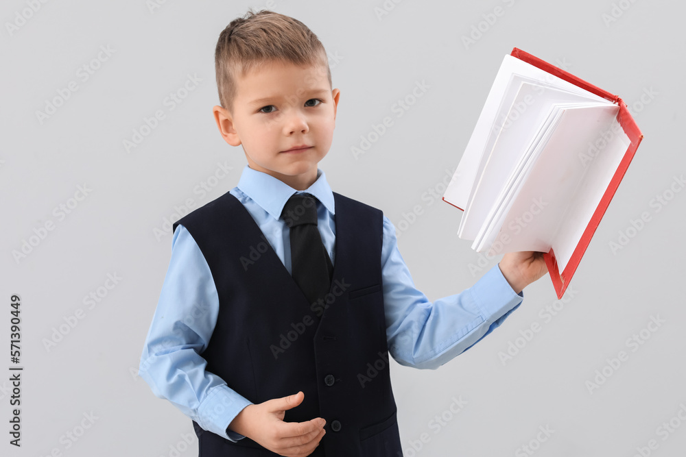 Cute little teacher with book on grey background