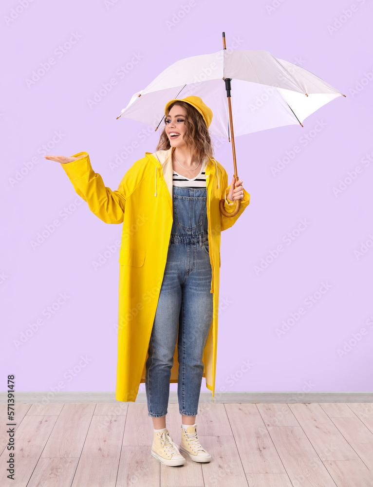 Stylish young woman in autumn clothes and with umbrella on lilac background