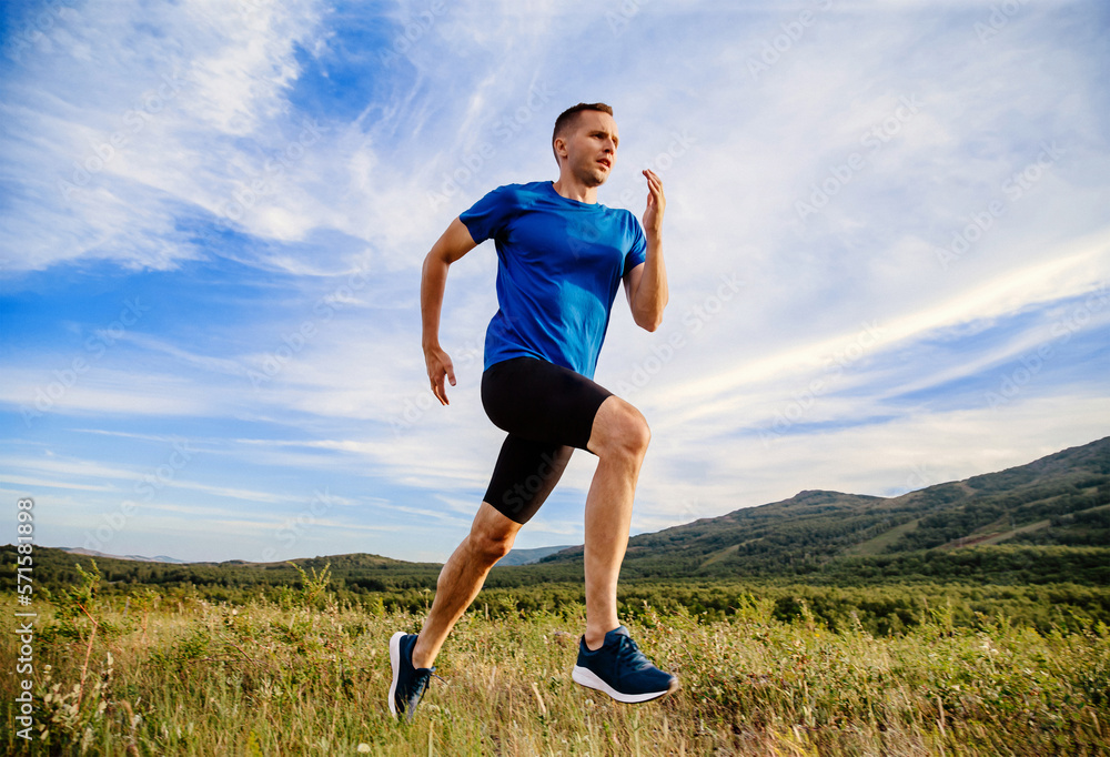 man runner running summer mountain meadow in background blue sky