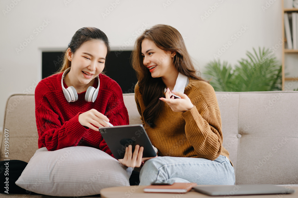 Two asian students learning together online with a laptop, tablet and tutor together in liveing room