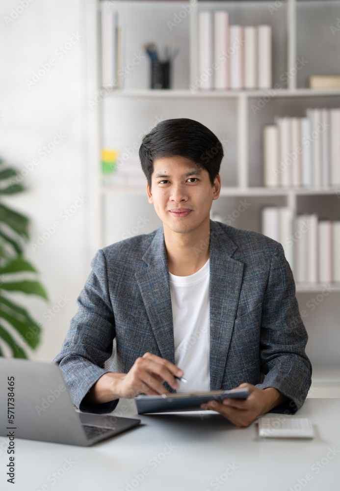 Young confident businessman working in the office room, smiling and looking at the camera.