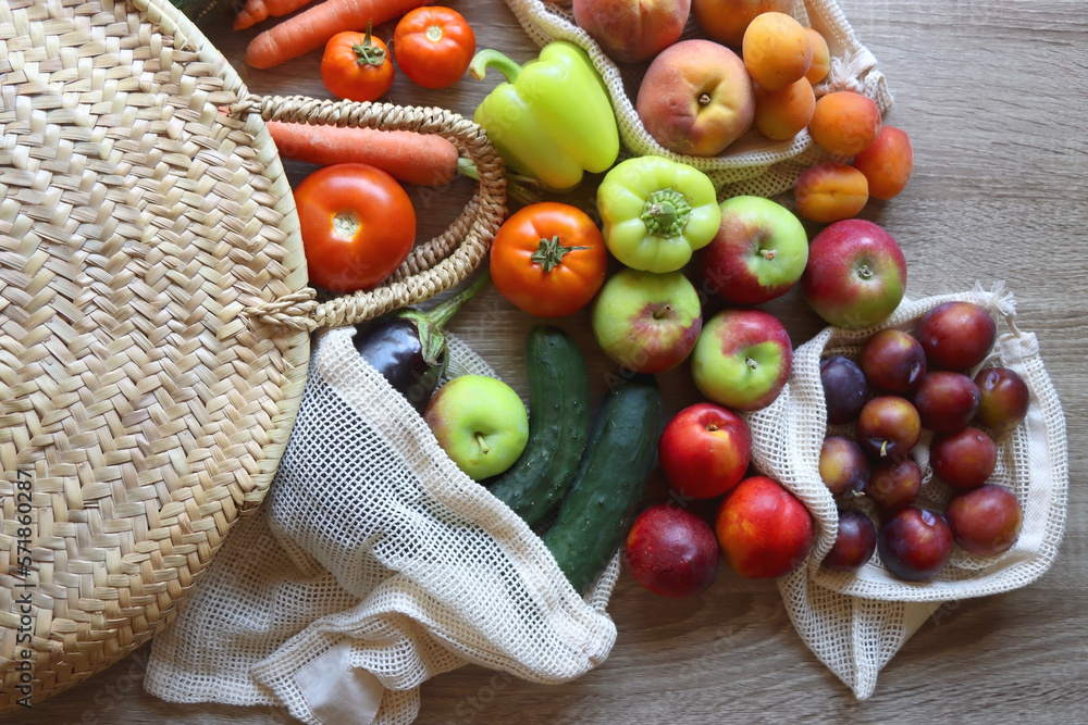 Straw bag and reusable fabric bags filled with various healthy fruit and vegetables. Wooden backgrou