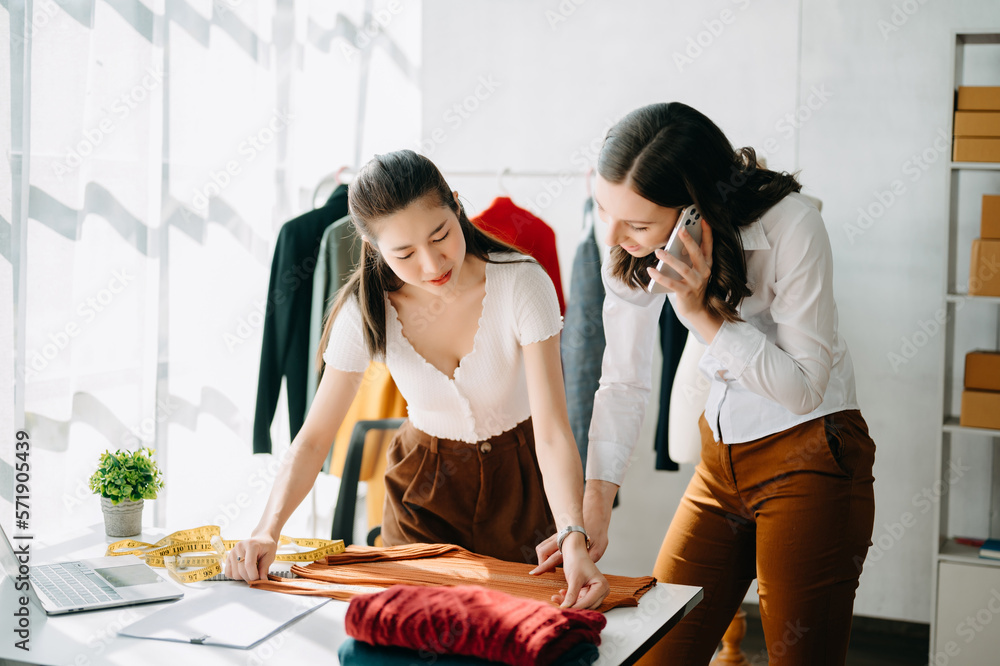 Couple of fashion designers working with fabric and clothing sketches at the studio full of tailorin