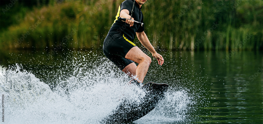 man wakeboarder on lake behind boat. water splashes from under board