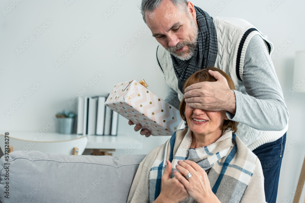 Caucasian senior elderly man surprise his wife with birthday gift at home