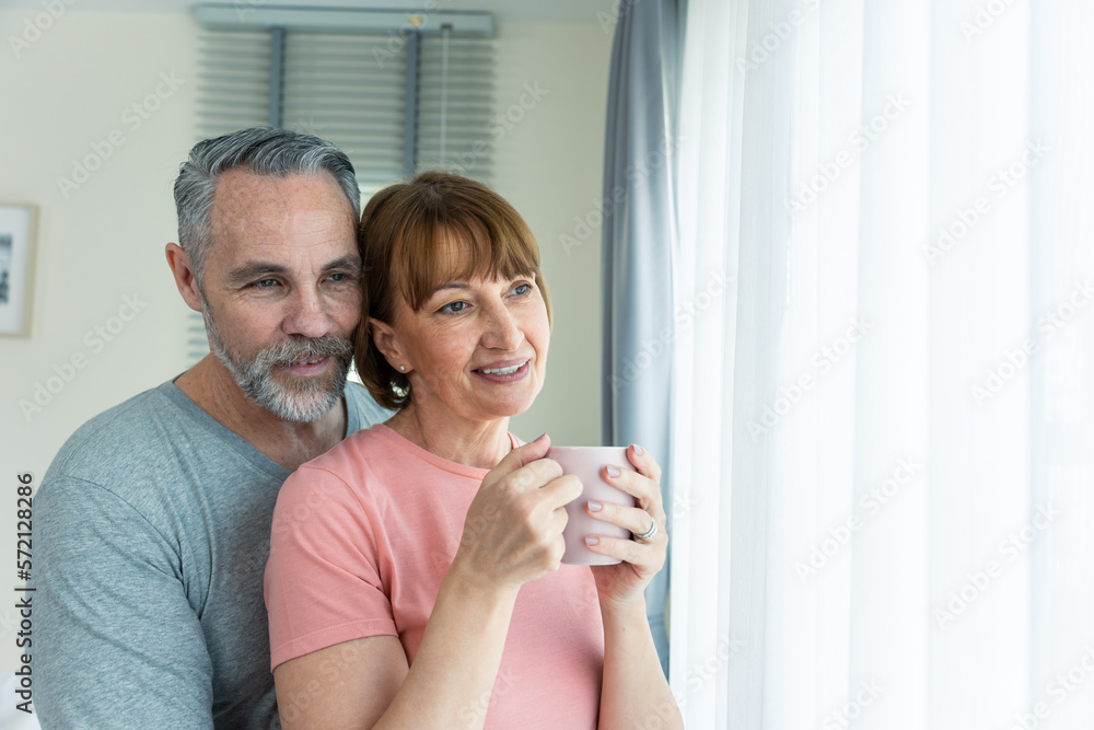 Caucasian senior older couple hugging each other in bedroom at home.