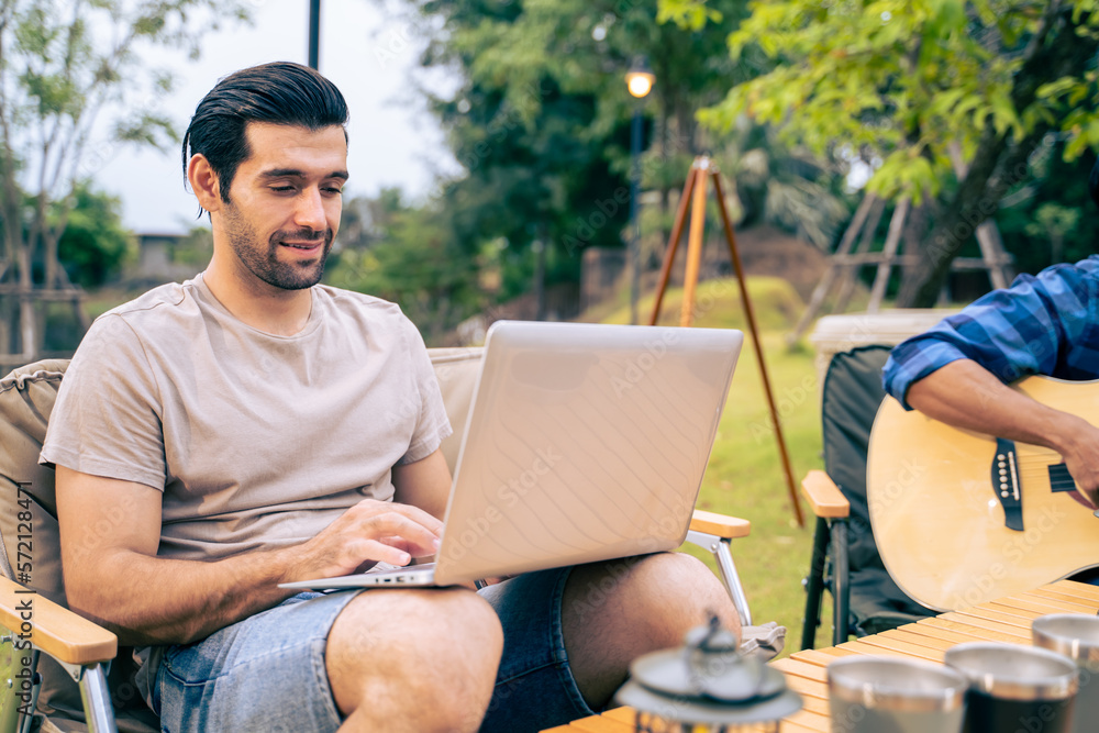 Caucasian handsome male working while having outdoors camping party. 