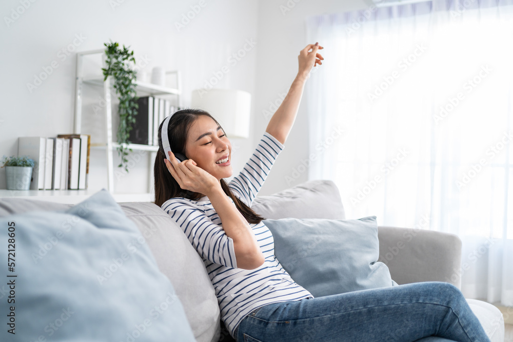 Asian woman listen to music and dancing while sitting on sofa house. 