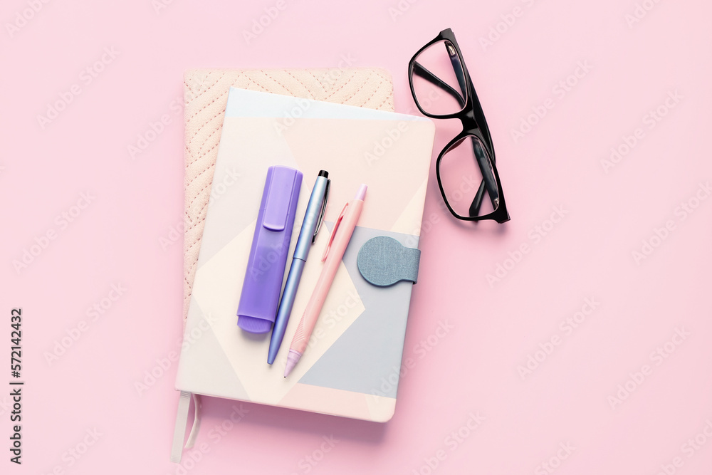 Notebooks, pens, marker and eyeglasses on pink background