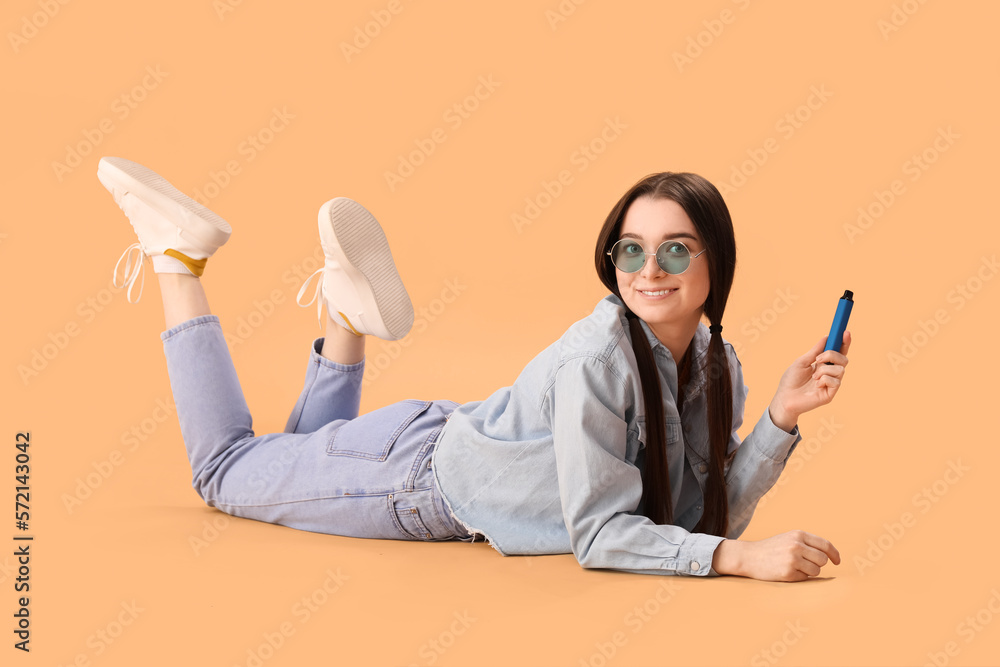 Young woman in sunglasses with disposable electronic cigarette lying on beige background