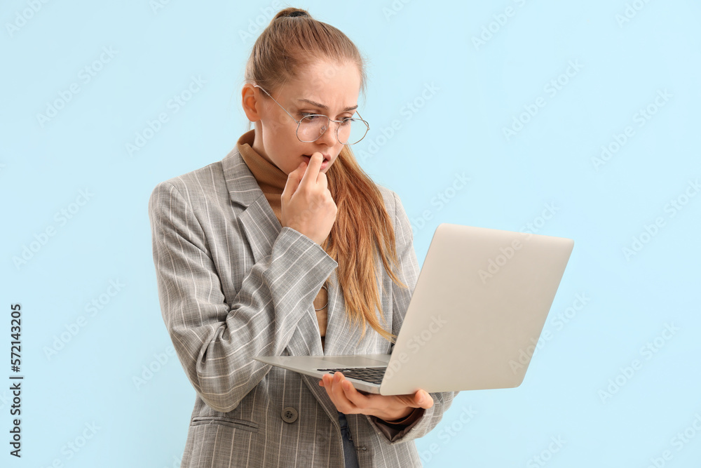 Young businesswoman with laptop biting nails on blue background