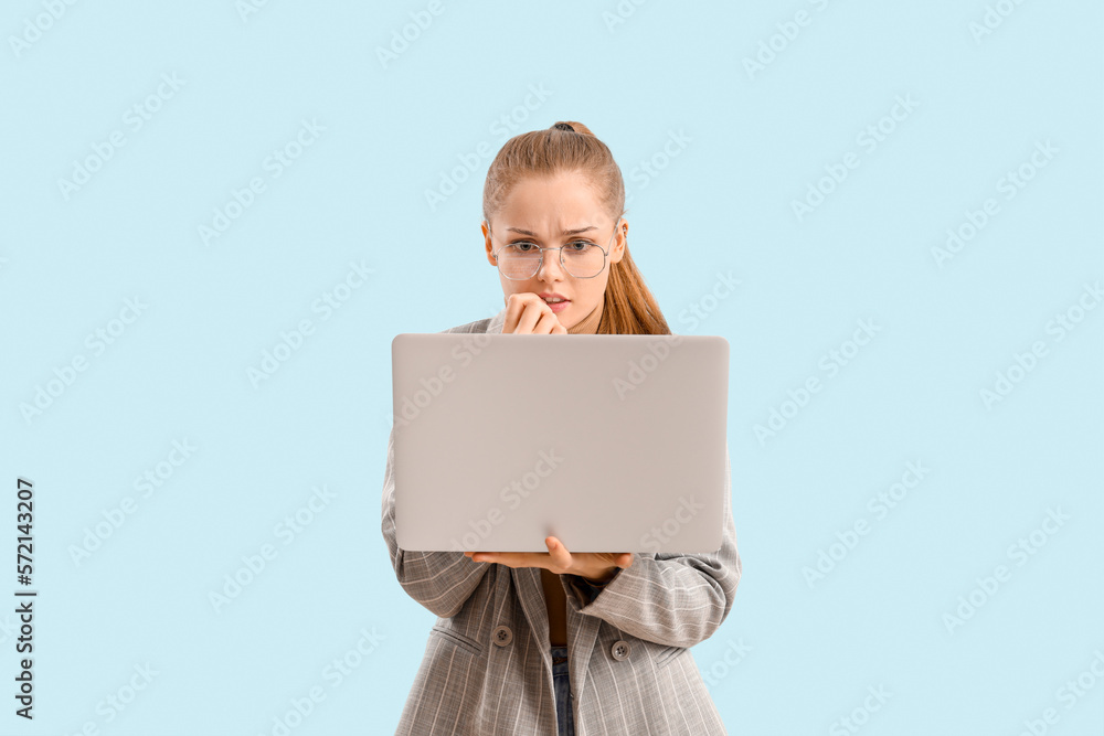 Young businesswoman with laptop biting nails on blue background