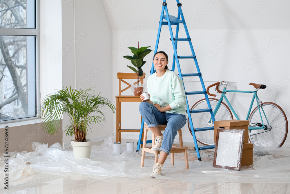 Young woman with paint can sitting on stepladder at home