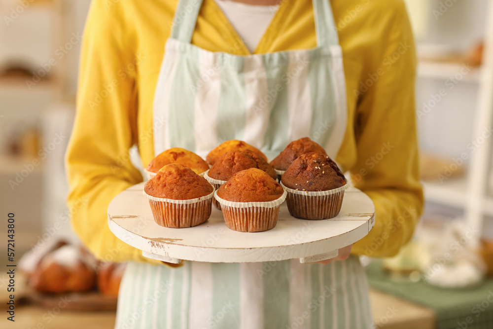 Female baker with tray of tasty cupcakes in kitchen, closeup