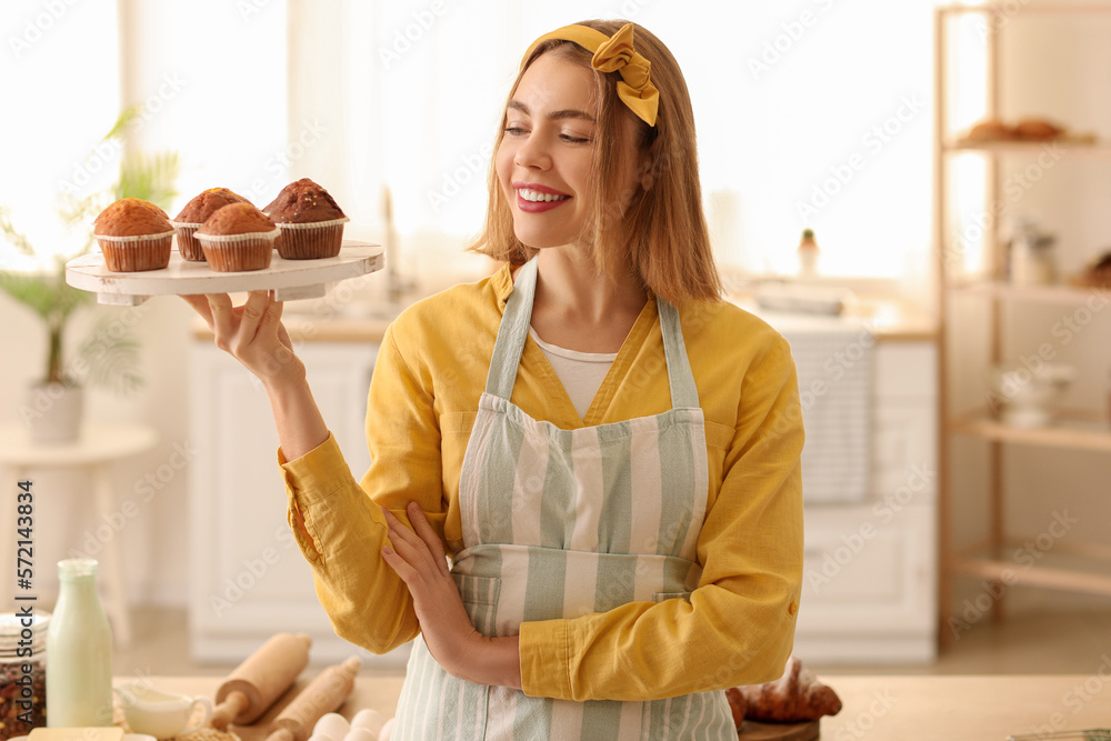 Female baker with tray of tasty cupcakes in kitchen